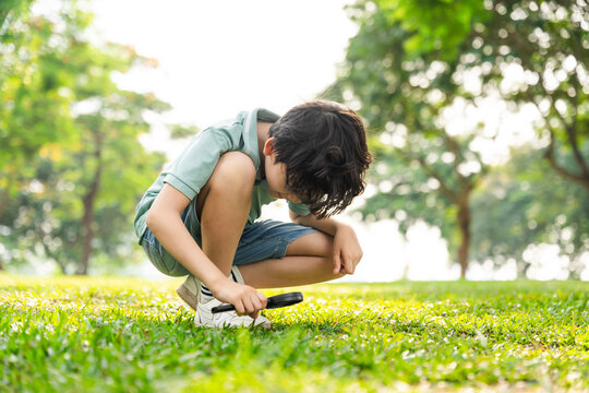 image of asian boy using magnifying glass in park