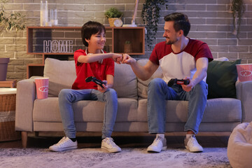 Little boy with his father bumping fists while playing video game at home in evening