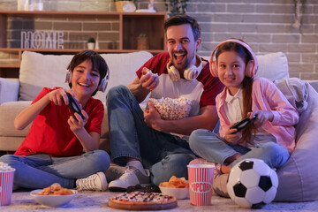 Father eating popcorn while his little children playing video game at home in evening