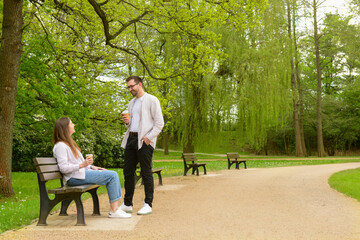 Beautiful loving couple sitting on bench and drinking coffee in park