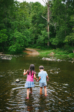Two children holding hands wade into the Eno River in Durham, North Carolina