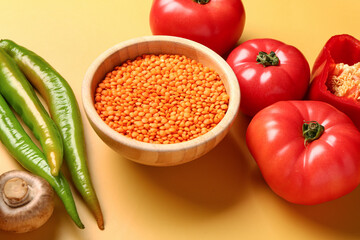 Different fresh vegetables and bowl with lentils on yellow background