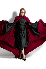 Naklejka premium Mysterious woman in black dress and flowing red cape with dramatic makeup and dark expression on white background