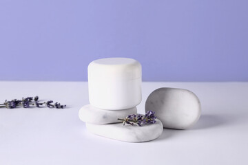 Jar of cosmetic product, spa stones and lavender flowers on light table against color background