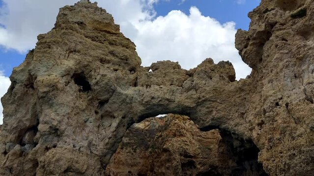 Bottom up shot sandstone cliff formation with different caves and peaks at Algarve against clouds at sky - Tilt down view from boat