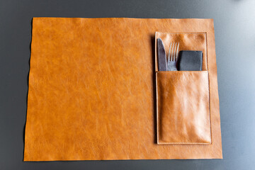 Brown leather table mat with fork and knife utensils on dark table top