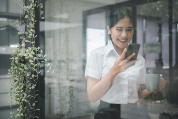 Attractive young woman talking on the smart phone and smiling while standing in office and looking smart phone.