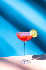Siesta alcoholic cocktail drink with silver tequila, grapefruit and lime juice, syrup and italian red bitter liqueur, summer blue bright background, hard light and shadows