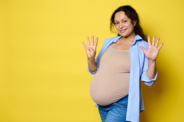 Cheerful pregnant woman expecting a baby, showing number nine with her fingers, 9 month of happy...