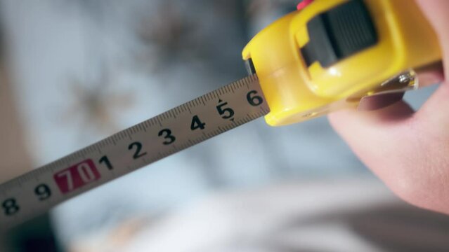 Metal industrial construction tape centimeter measure close up. Male hands pull the measuring tape out of tape measure and measure the length or width dimensions.