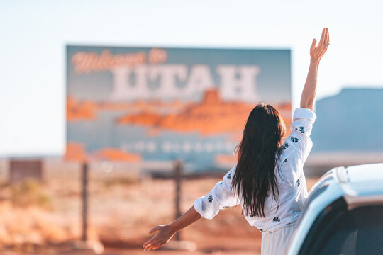 Beautiful woman on her trip by the car on the background of Welcome to Utah state border sign right in the Monument Valley