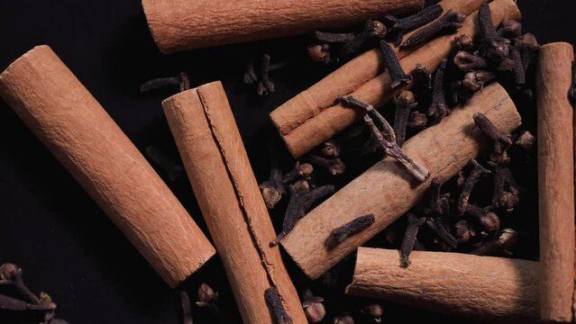 Fragrant spices, cinnamon sticks, dried cloves rotating on a black background close-up of slowmo.