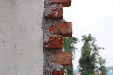 An under construction white wall with red bricks on its end and few trees in a blurred background 