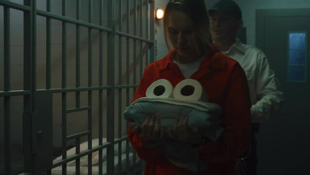 Prison officer leads female prisoner in orange uniform to prison cell, locks inside, puts off handcuffs. Women serve imprisonment terms for crimes in jail. Detention center or correctional facility.