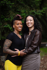 Wrapped in each other's arms, a couples smiles together. Adding narrative, they self-identify as queer, and are lesbian and multiracial. They are facing each other, expressing their closeness.