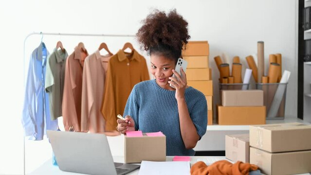 Startup small business SME, Entrepreneur owner African woman using smartphone or tablet taking receive and checking online purchase shopping order to preparing pack product box. .