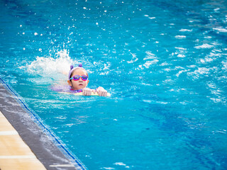 Asian child or kid girl wearing swimming suit to learning on swimming pool , learn and training swim on kick board