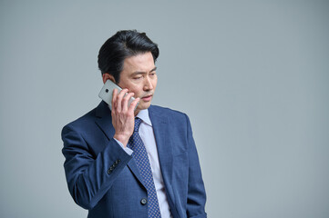 A middle-aged office worker in a suit is holding a smartphone and making various emotional expressions.