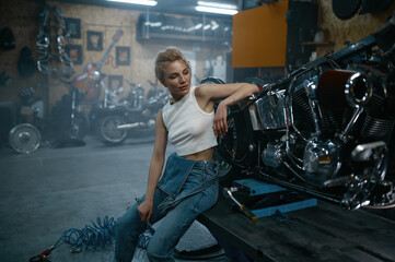 Fototapeta na wymiar Attractive woman mechanic posing for camera at motorcycle garage