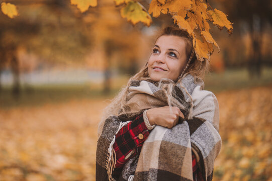 Portrait Middle-aged woman enjoys autumn warm weather. Mature blond woman in a plaid plaid with a bouquet of yellow leaves in the park in autumn