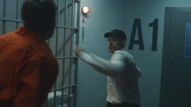 Male prisoner in orange uniform fights with jailer near prison cell. Prison worker attacks and hits criminal with police baton. Escape from jail. Fighting in detention center or correctional facility.