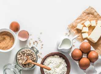 Baking ingredients background - oat flakes, flour, cane sugar, butter, eggs on a light background, top view. Copy space