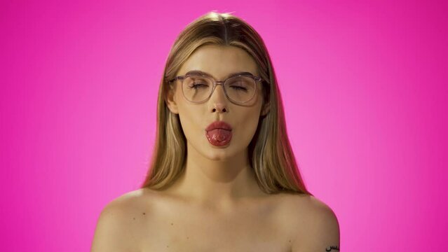 Cheeky young caucasian woman sticks tongue out, isolated purple background