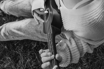 The girl is playing the ukulele in the park, resting and enjoying a warm day. Space for copying. Black and white picture.