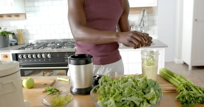 Midsection of african american man preparing healthy smoothie in kitchen at home, slow motion