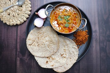Traditional Sev bhaji or sev tamatar nu Shaak with Jowar Bhakri. Sev is a crisp fried gram flour vermicelli. Served with chopped onion and lemon. with Copy space. Its a sweet and spicy indian curry.