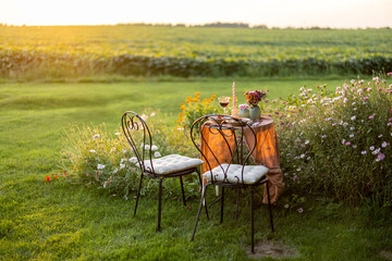 Beautiful green lawn with flowers and dining table for two during the sunset. Romantic picnic on nature