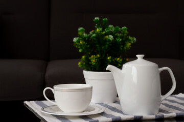 White coffee cup or teacup and jug with blurred flowerpot put on coffee table in the living room....