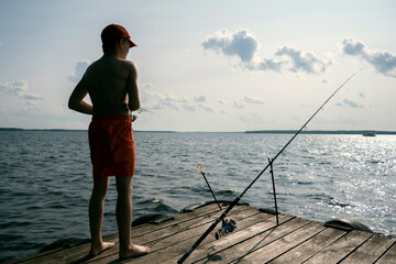 A teenager in red shorts and a red baseball cap fishes in the river. Summer vacation.