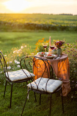 Beautiful green lawn with flowers and dining table for two during the sunset. Romantic picnic on...