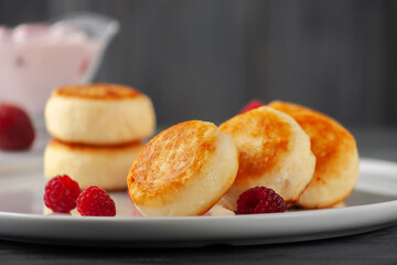Cottage cheese fritters or syrniki served with yogurt and raspberries, side view.