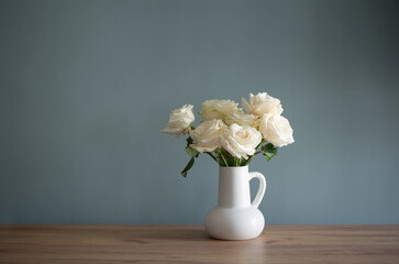 bouquet of white roses in jug in background blue wall