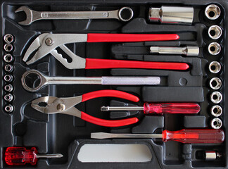 Pliers, screwdrivers, spanners and socket wrench and sockets in a black toolbox with separated slots top view