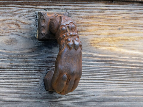 Antigua puerta de madera con aldaba de fundici&oacute;n, en el pueblo mallorqu&iacute;n de Deia, con forma de mano sobre la madera envejecida mostrando su textura
