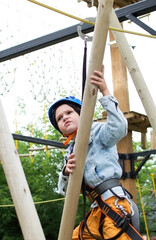 Fototapeta premium Child in forest adventure park. An outdoor entertainment center for children engaged in agility and rock climbing. Children enjoy spending time outdoors on warm sunny summer day. Vertical photography.