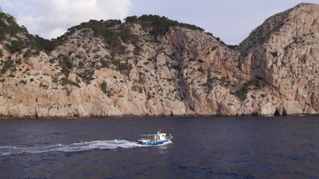 Side panning shot of fishing boat on small waves near Mallorca during sunrise, aerial