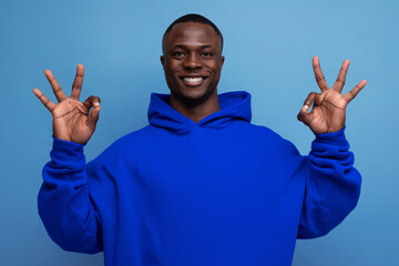 friendly dark-skinned young american man in blue sweatshirt on studio background with copy space