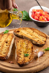 Pouring oil onto slice of toasted bread ready to make toasts. Food recipe background. Close up