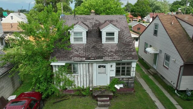 Rundown house with falling apart shingles on roof. Aerial rising shot of old home in USA. Summertime drone shot.
