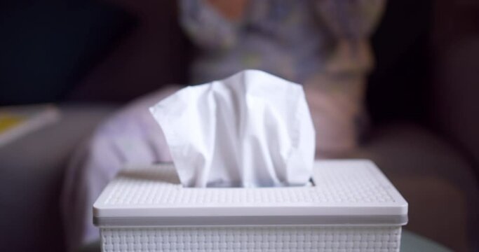 White paper tissue in a metal container box standing on a table outdoors in street sunny restaurant. Female hand takes one paper napkin blowing by the wind