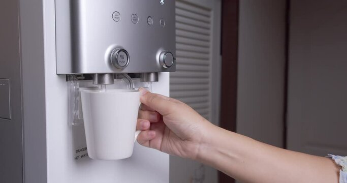 Woman presses a cup of hot water from the water purifier and put it back. Close up look at the glass cup in the kitchen.
