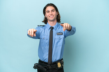 Young police caucasian man isolated on blue background points finger at you while smiling