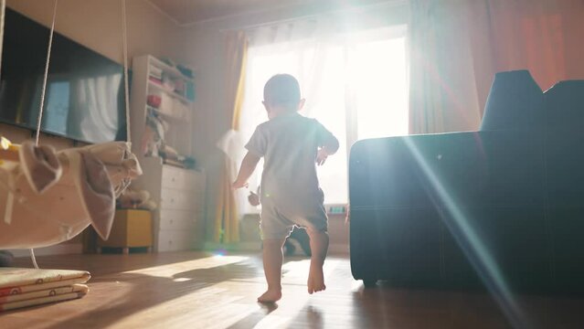 baby toddler first steps. baby son takes the first steps around the room to his father sitting by the window glare of the sun learns to walk. happy family kid concept. toddler first steps dream