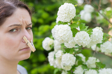 Unhappy woman with a clothespin on her nose on a walk in a blooming park.  - obrazy, fototapety, plakaty