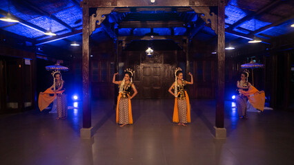a group of Javanese dancers in yellow shawls dance in front of a blue light
