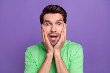 Photo of funny young guy touch cheekbones surprised impressed reaction wear trendy t-shirt unexpected news isolated on purple background